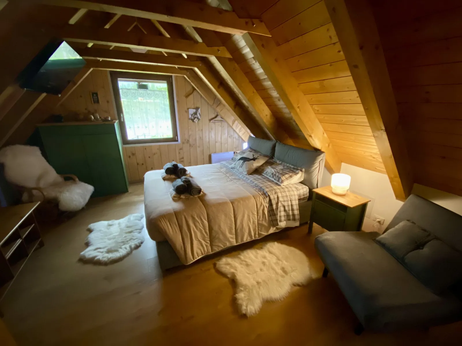 Schlafzimmer unterm Dach mit Holzwänden, Doppelbett und Sofa.