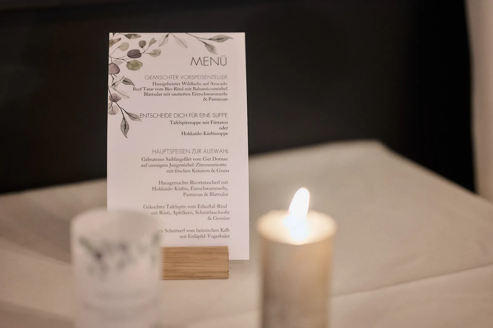 Menükarte in einem Holzhalter neben einer brennenden Kerze auf dem Hochzeitstisch.