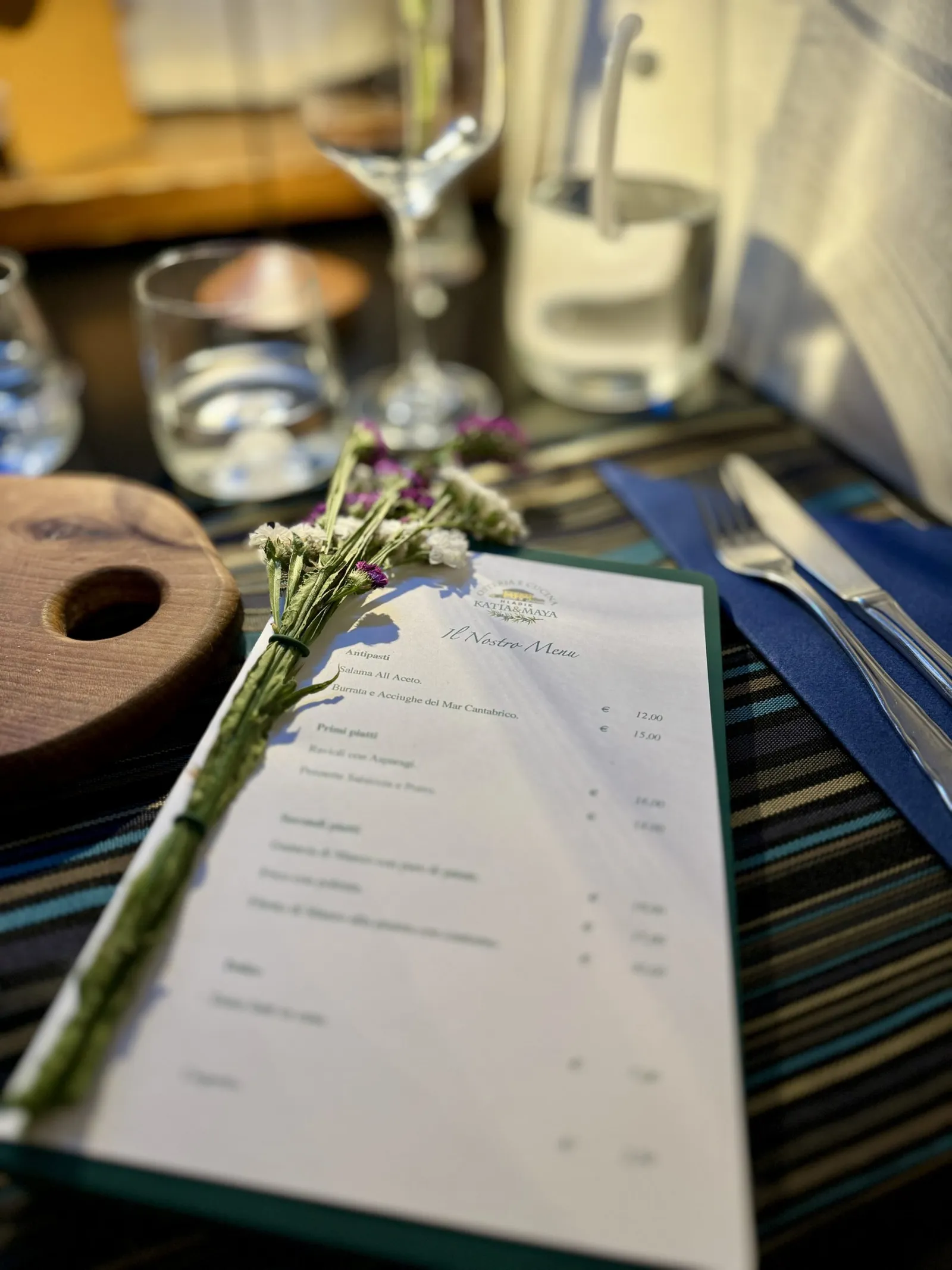 Menükarte der Osteria Hladik auf einem gedeckten Tisch mit Gläsern und Besteck.