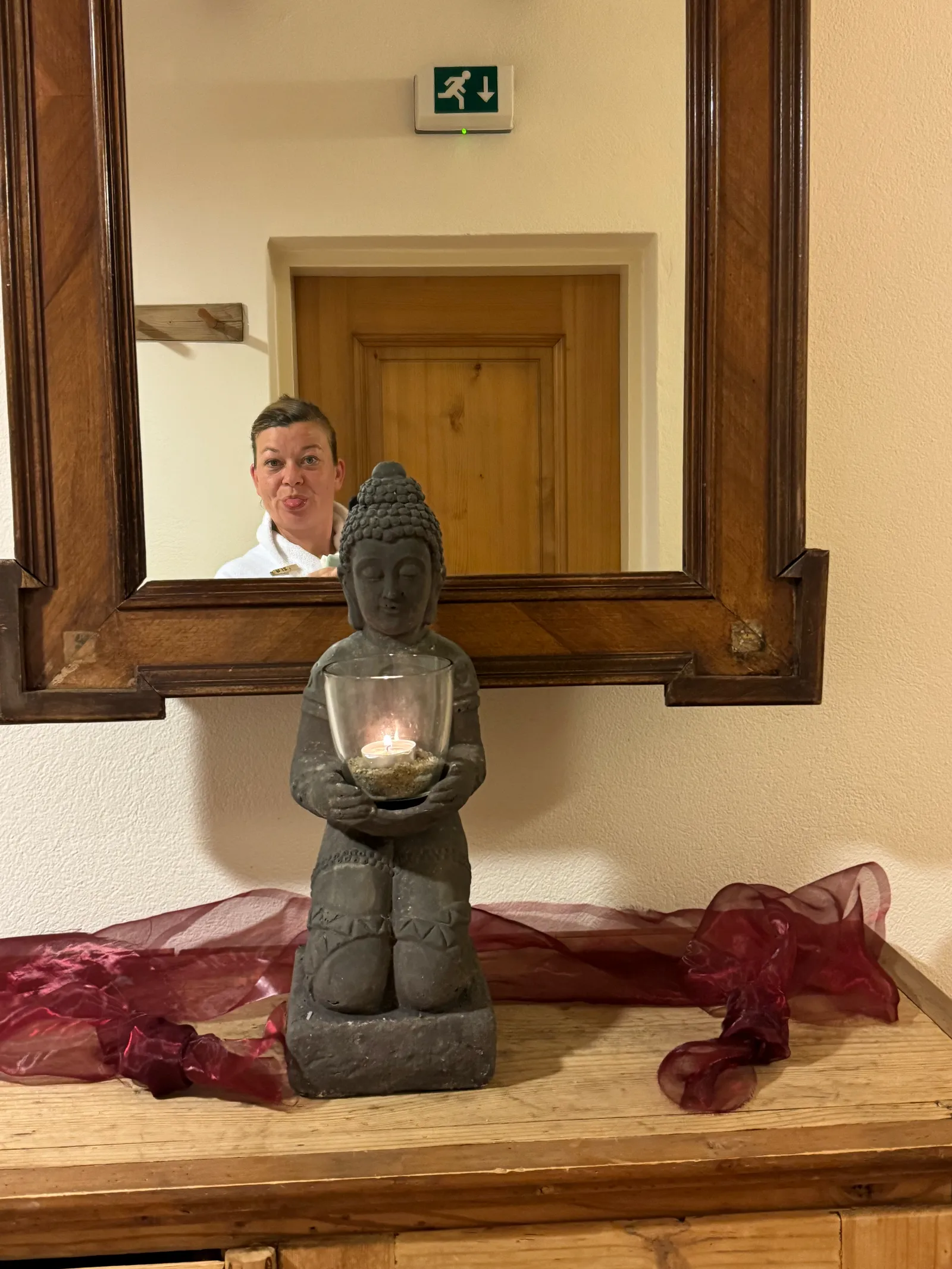 Buddha-Figur mit brennender Kerze auf einer Kommode, im Spiegel dahinter spiegelt sich eine Frau.