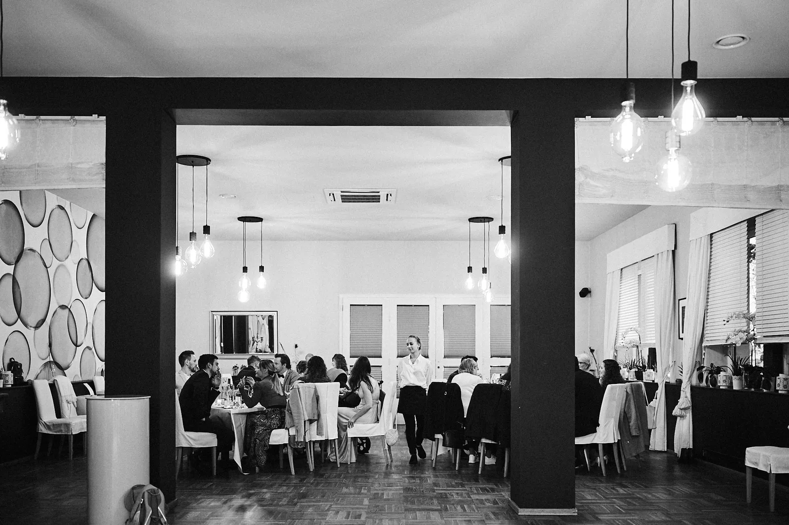 Schwarzweißaufnahme einer Hochzeitsgesellschaft beim Festessen in einem Restaurantsaal.