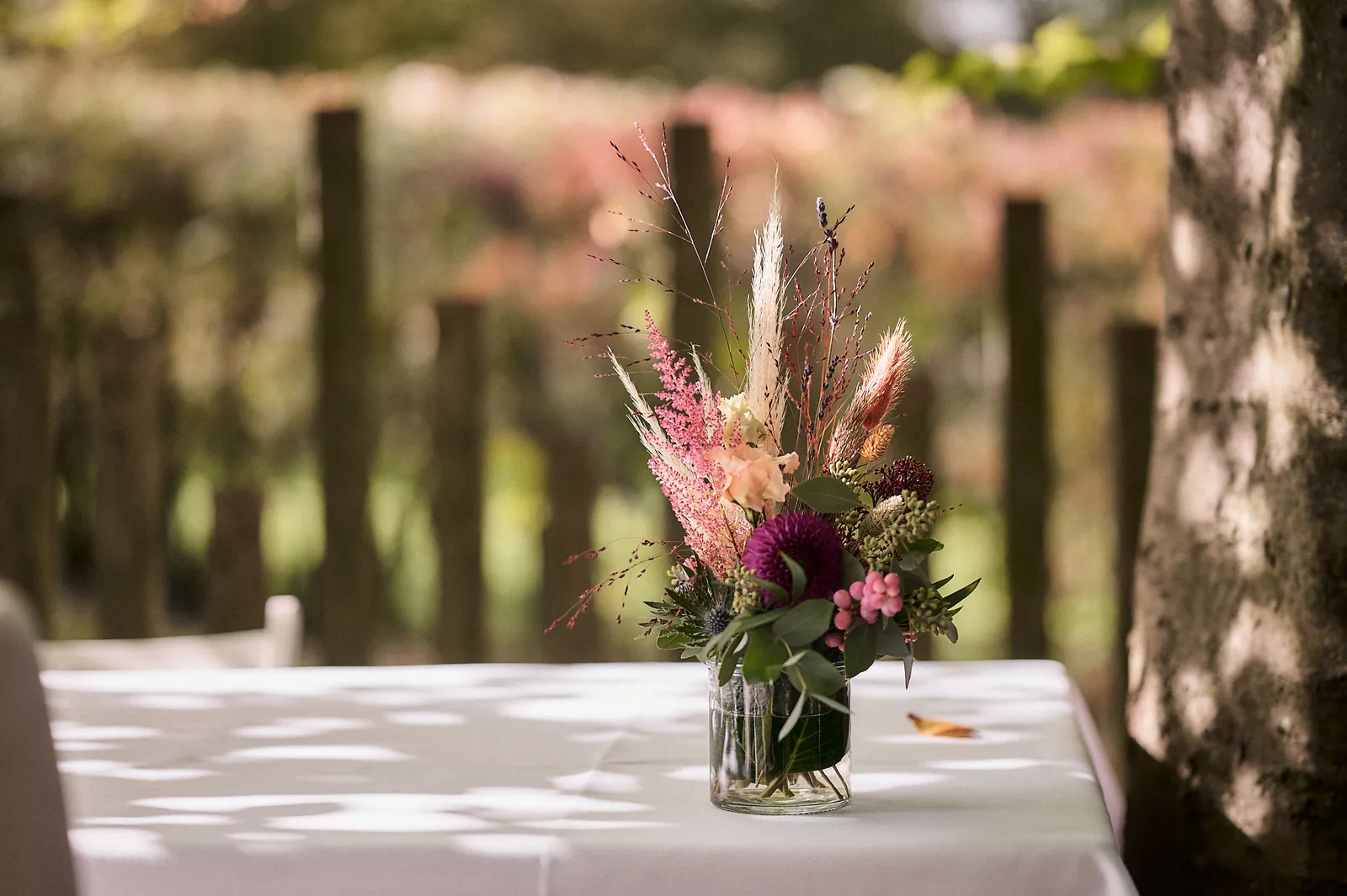 Kleiner Blumenstrauß mit pinken Blüten und Pampasgras in einem Glas auf einem Tisch im Freien.