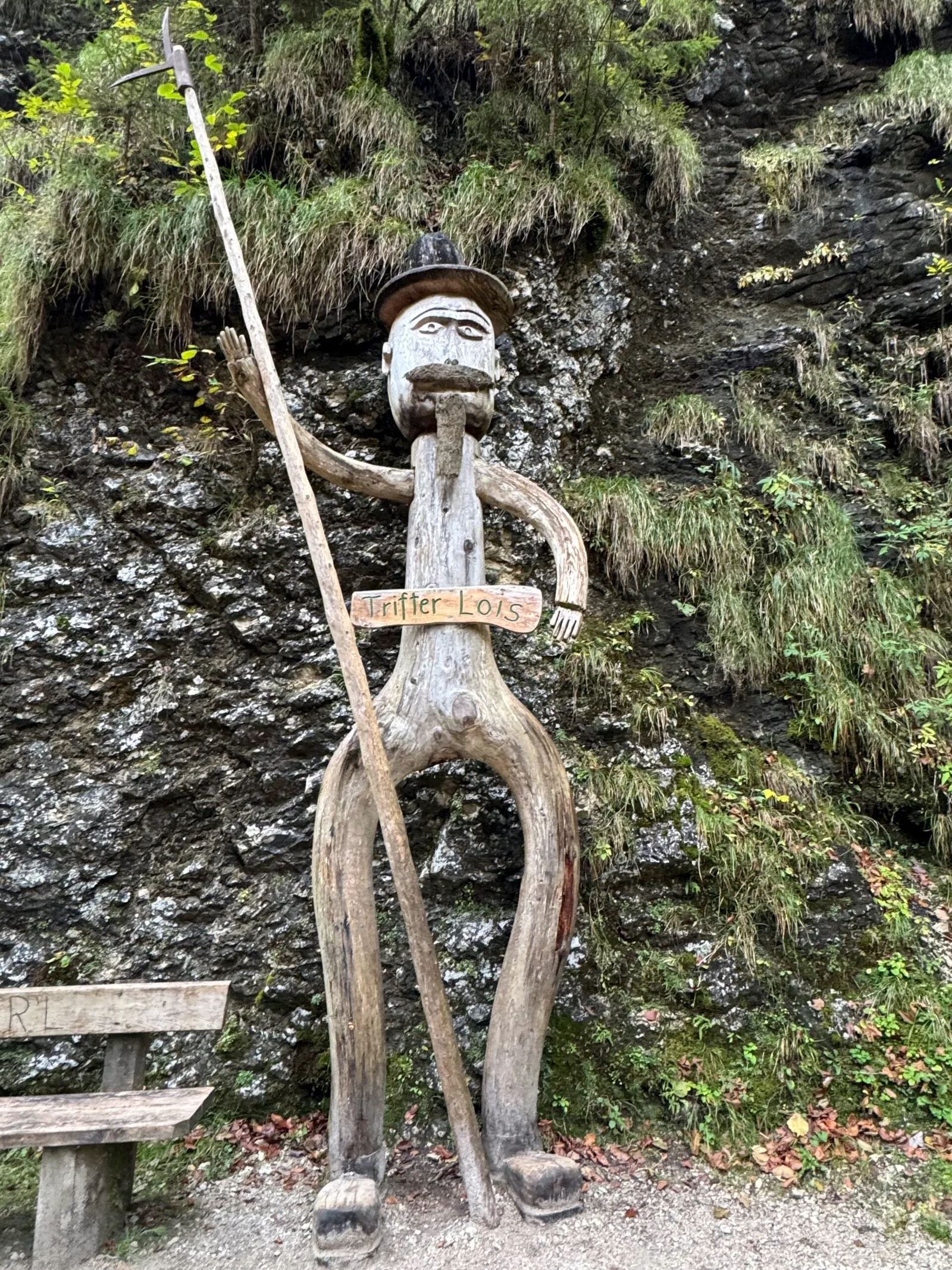 Hölzerne Figurenskulptur „Trifter-Lois" vor einer bemoosten Felswand im Mendlingtal.
