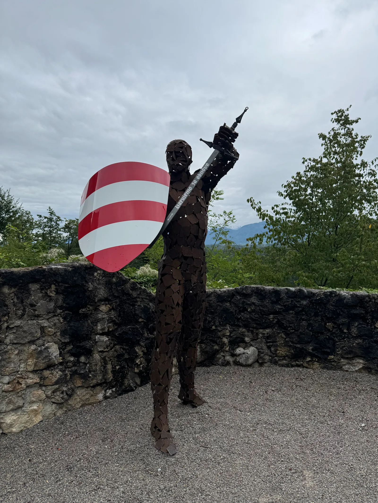 Metallskulptur eines Ritters mit Schwert und rot-weiß gestreiftem Schild auf der Burgmauer von Grad Žovnek.