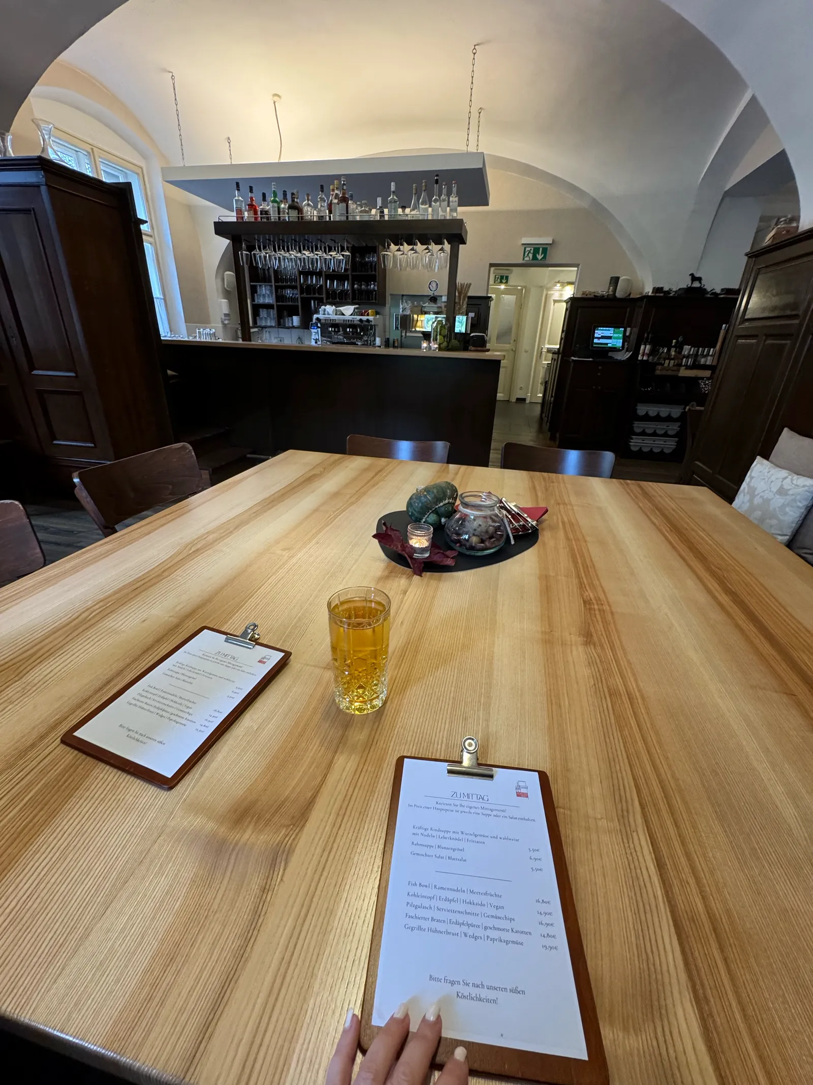 Holztisch mit Speisekarten im Gewölberestaurant von Schloss Rothschild, Bar im Hintergrund.
