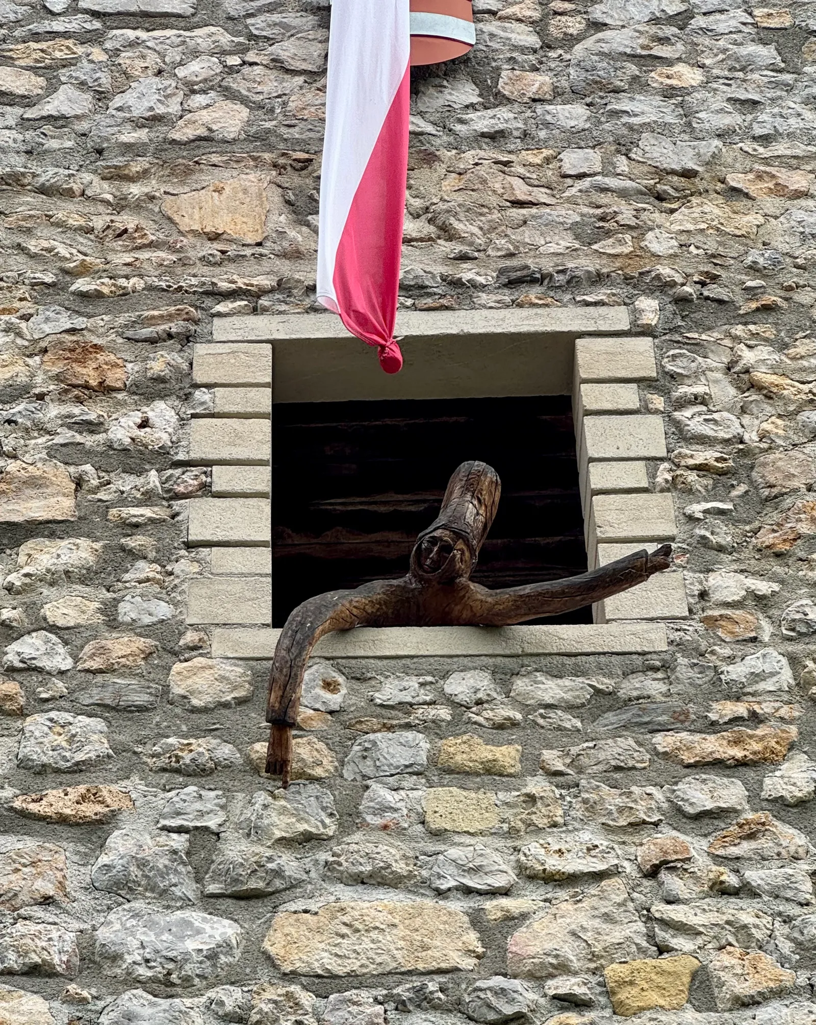 Eine hölzerne Figur schaut aus einem Mauerfenster der Burg Žovnek, darüber hängt eine rot-weiße Fahne.