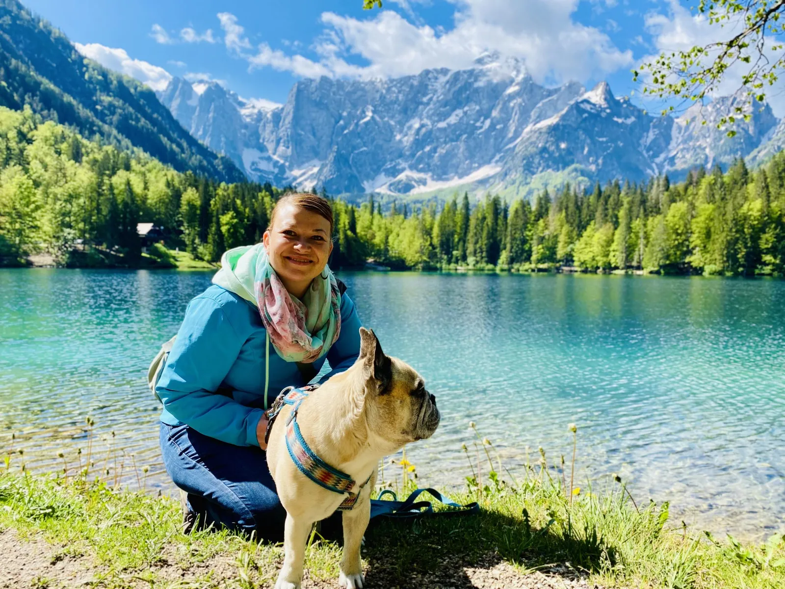 Babsi und Murphy am Ufer eines türkisen Bergsees mit Schneebergen im Hintergrund.
