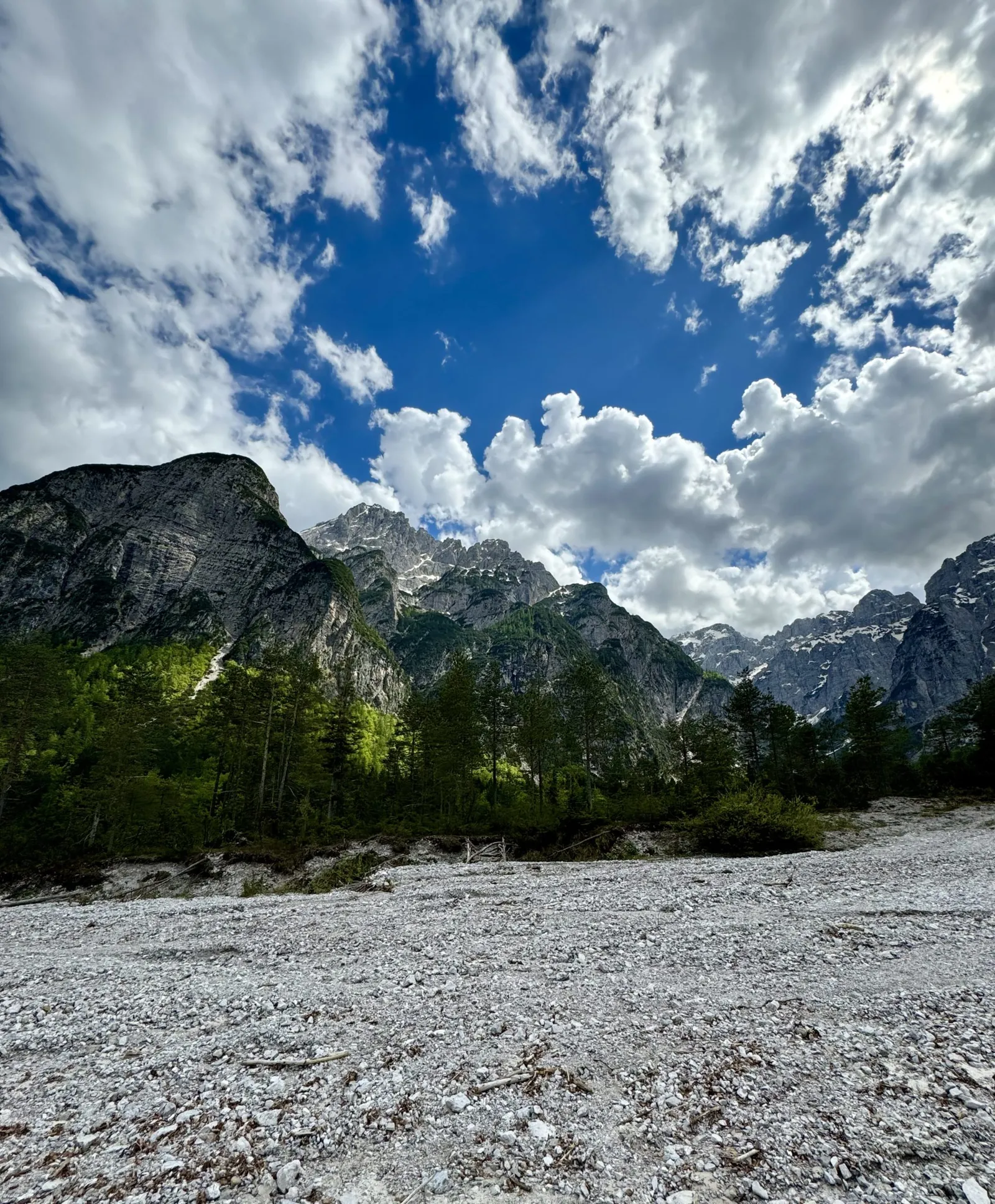 Steiniges, trockenes Flussbett im Val Saisera vor einem Bergpanorama mit bewölktem Himmel.
