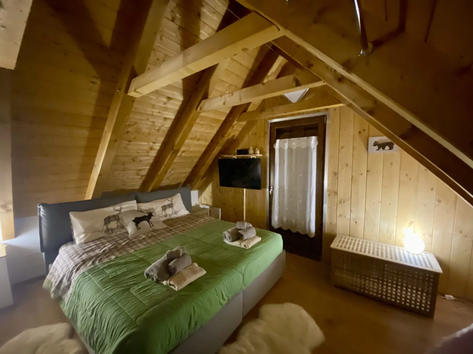 Schlafzimmer unterm Dach mit grüner Tagesdecke und Holzwänden.