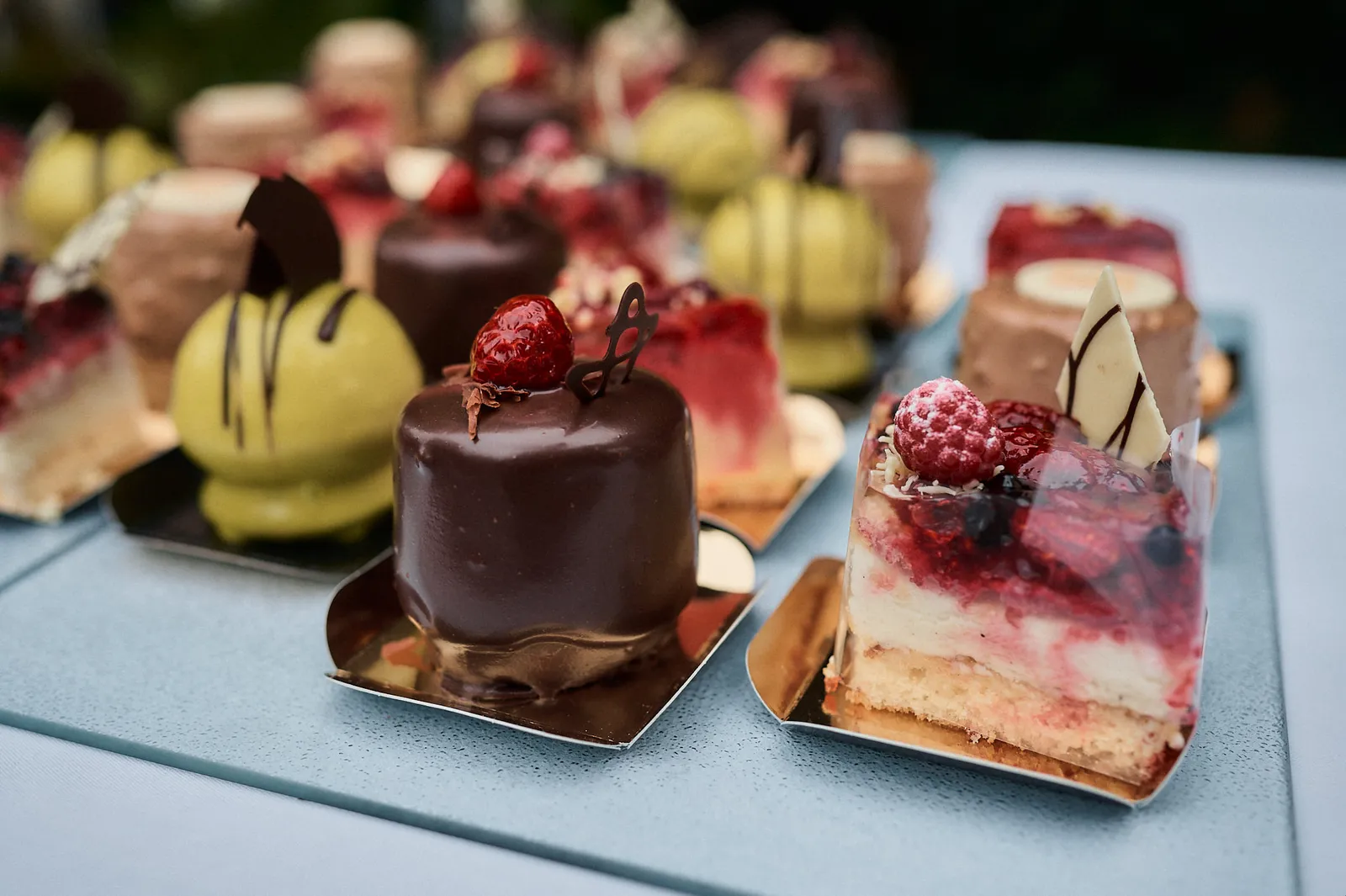 Mehrere kleine Törtchen mit Schokoladenglasur und Beeren auf einem Tisch nebeneinander.