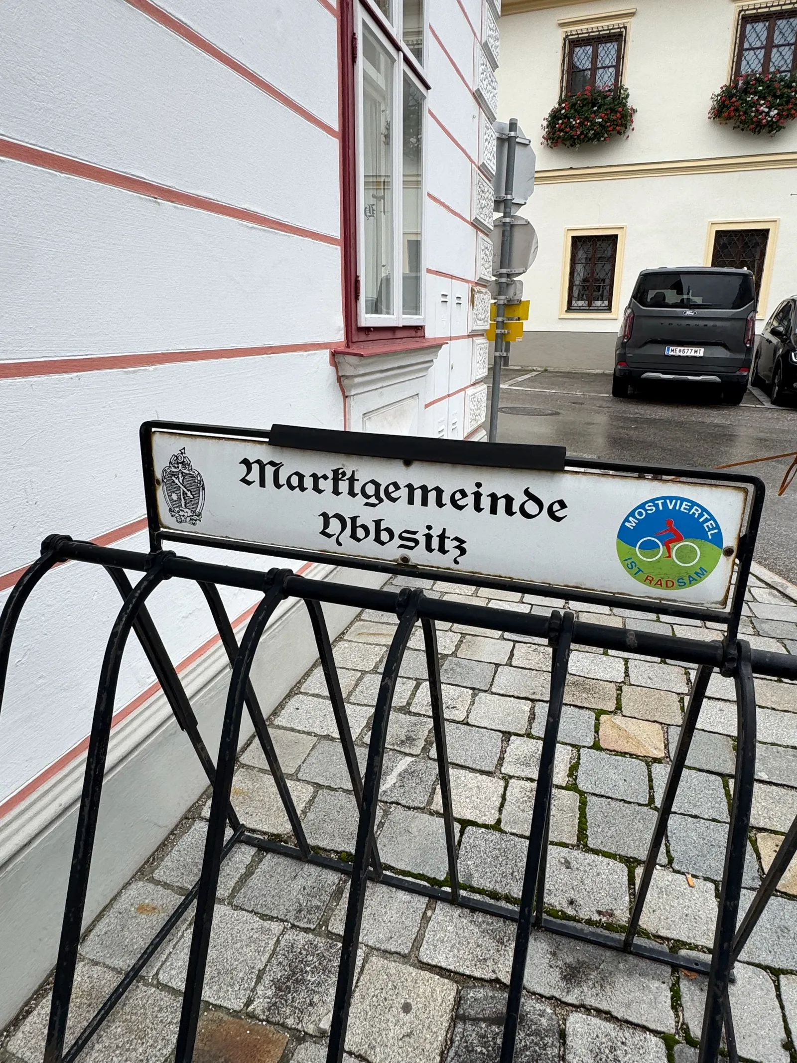 Ortsschild der Marktgemeinde Ybbsitz an einem schmiedeeisernen Ständer vor einem Gebäude.