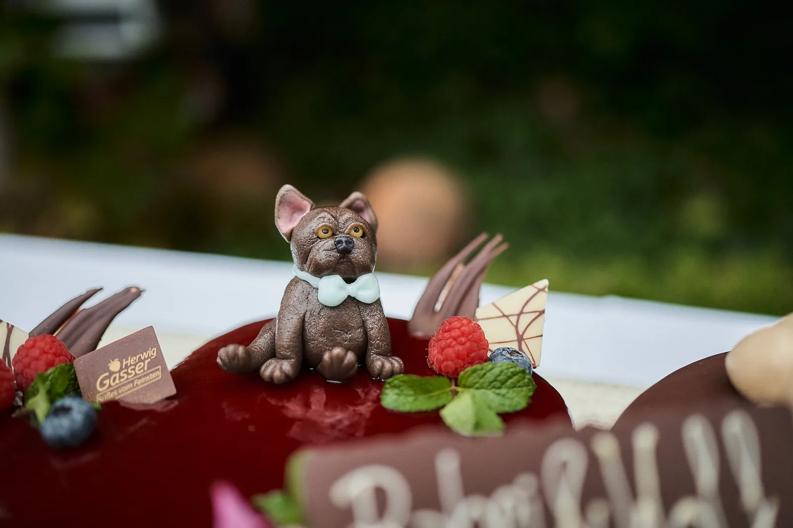 Nahaufnahme einer dunklen Schokoladen-Hundefigur mit Fliege auf der Hochzeitstorte.