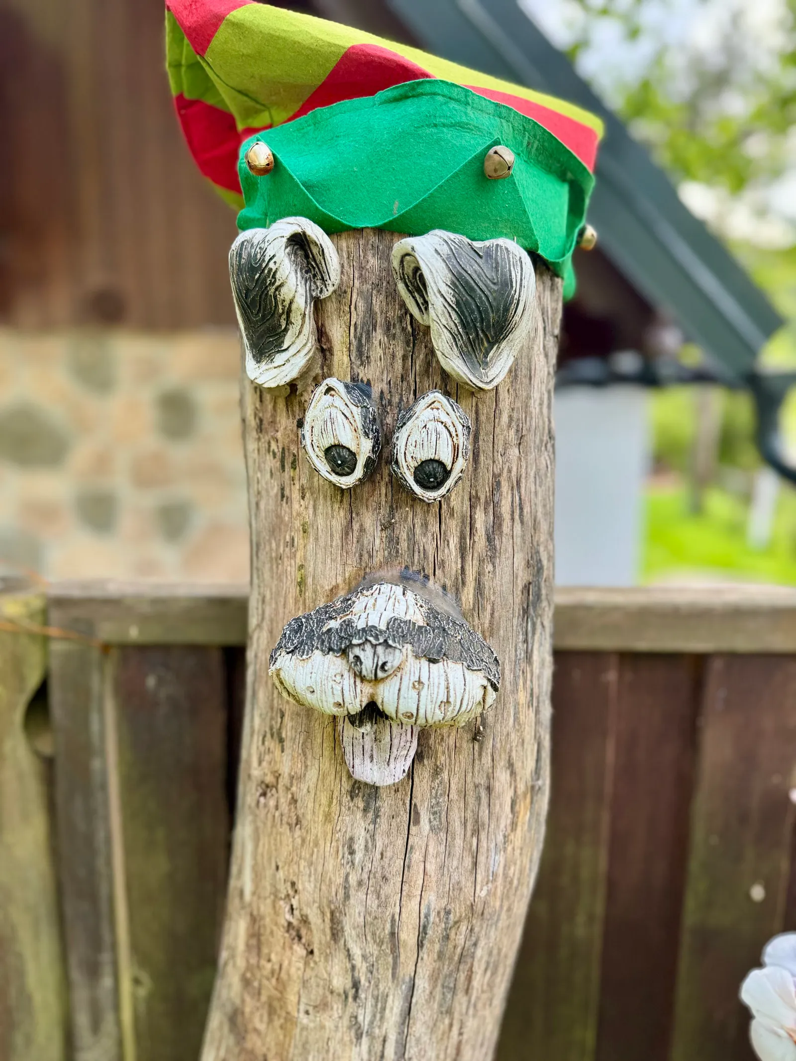 Hölzerner Zaunpfahl mit einem aus Naturmaterialien gestalteten Hundegesicht und buntem Hut.