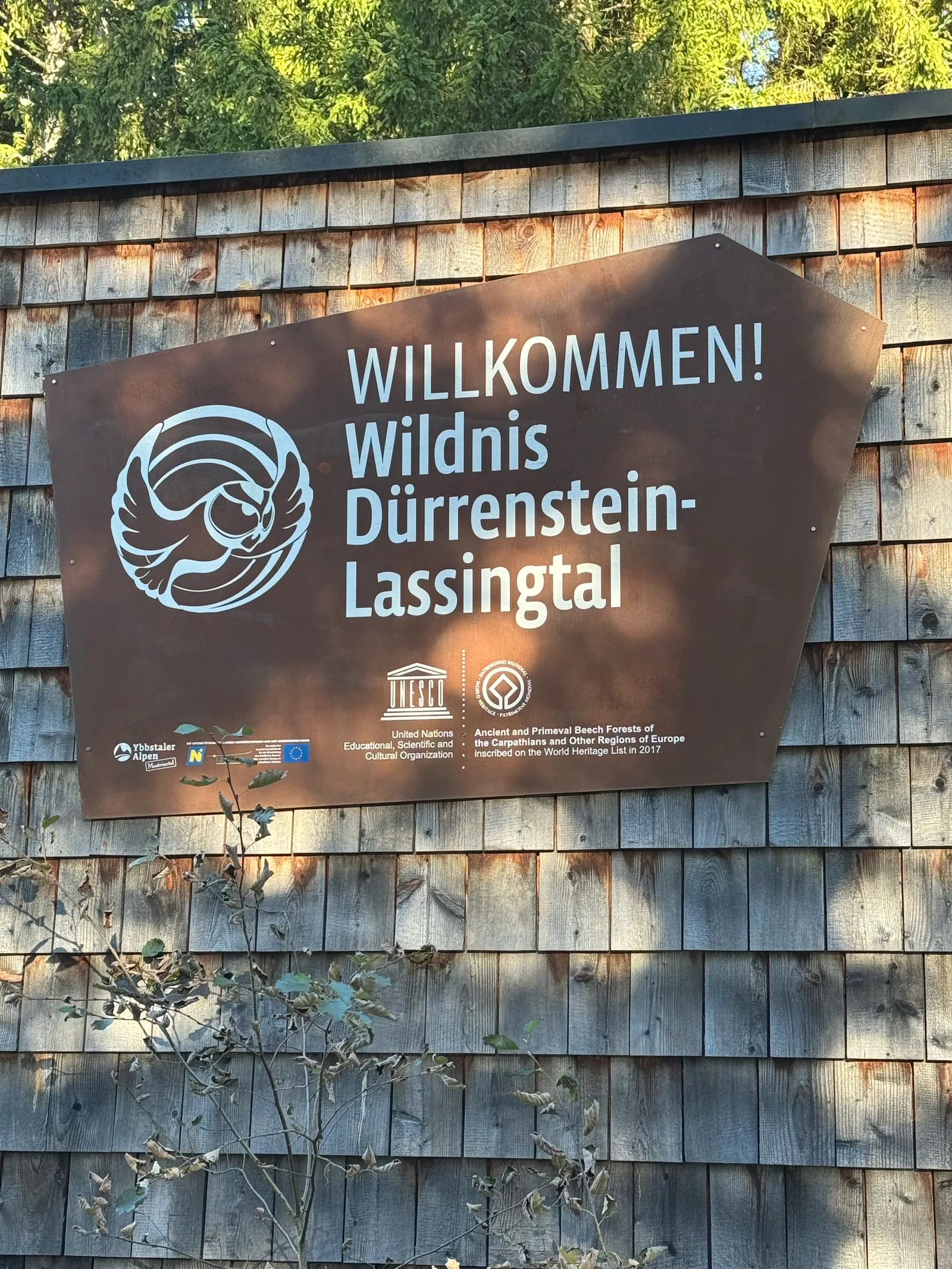 Willkommensschild der Wildnis Dürrenstein-Lassingtal mit UNESCO-Logo an einer Holzschindelfassade.