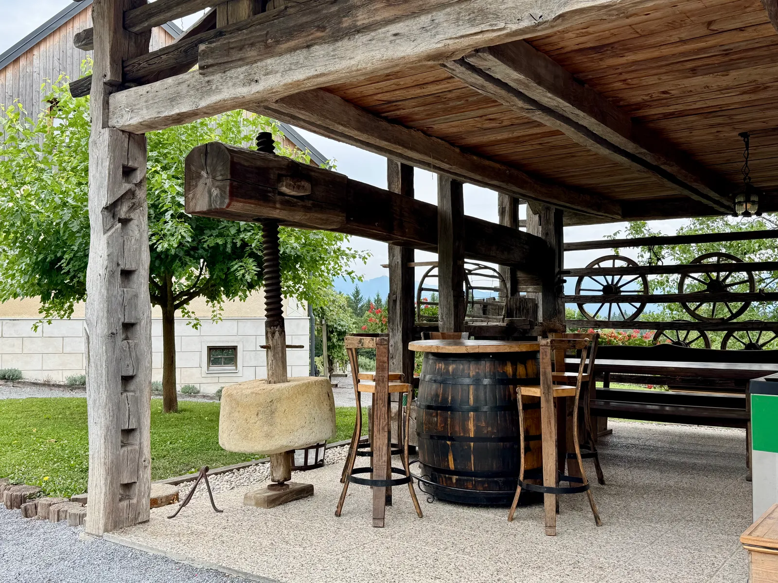 Überdachter Außenbereich mit alter Weinpresse, Holzfässern als Stehtische und Wagenrädern als Dekoration.