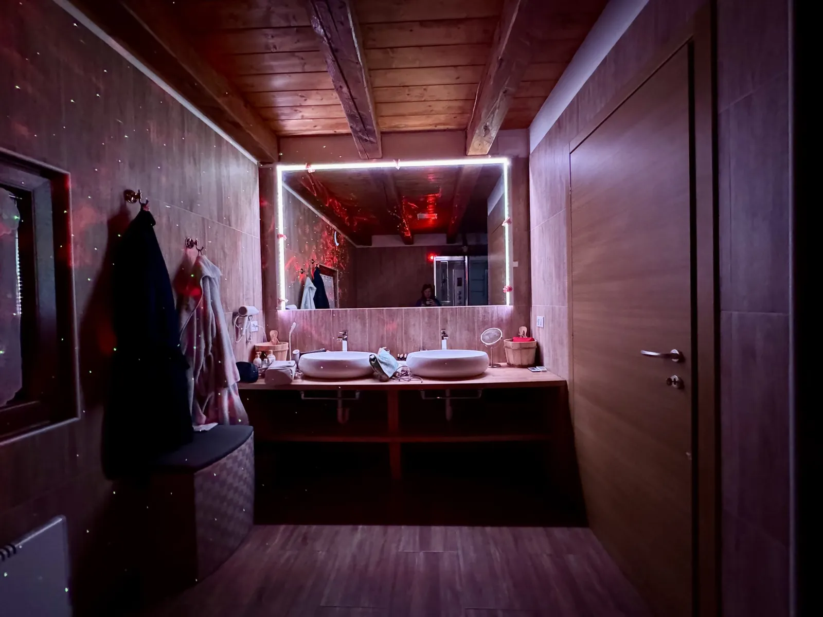 Badezimmer mit Doppelwaschbecken und großem hinterleuchtetem Spiegel in warmem Rotlicht.