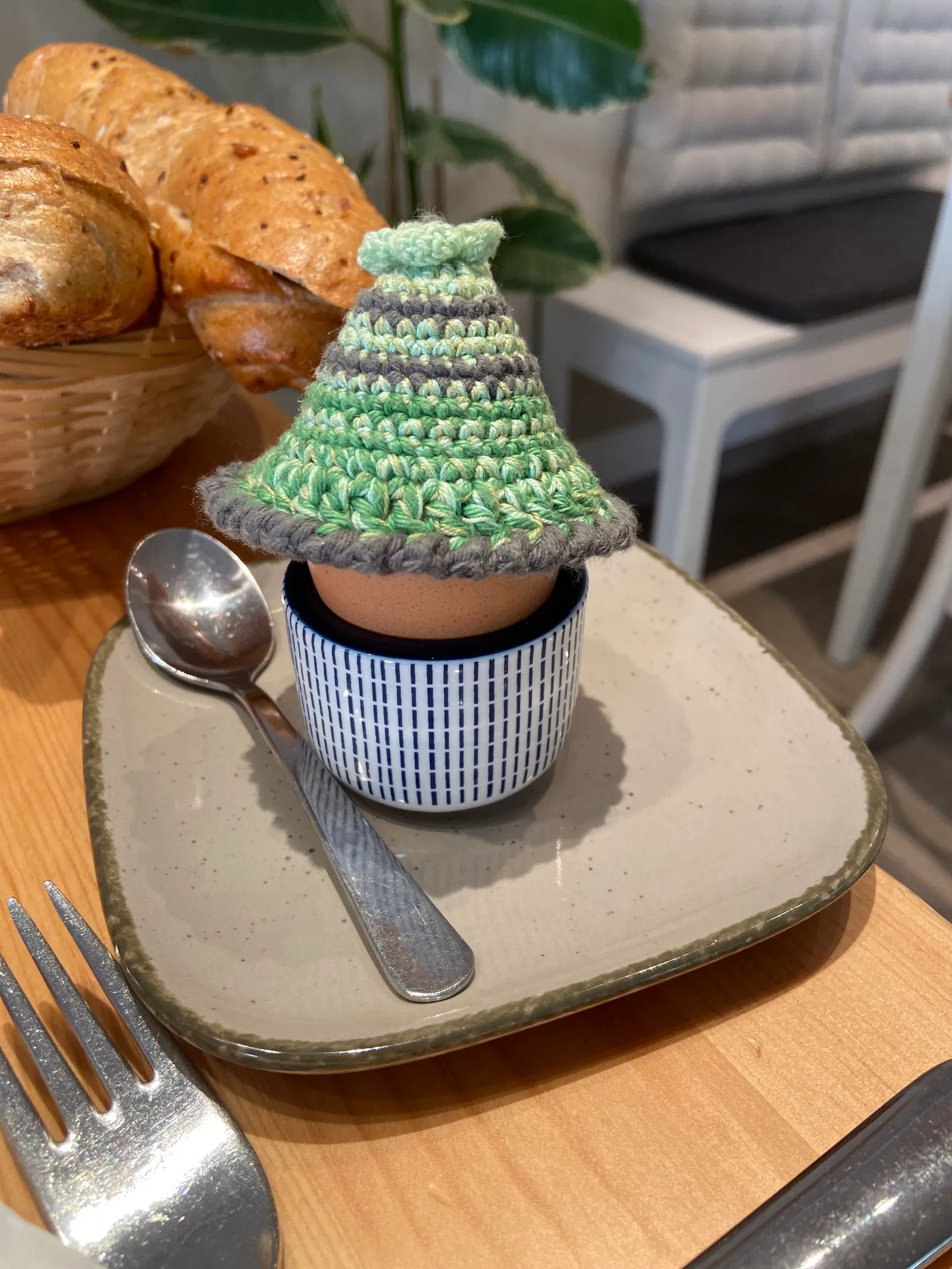 Ein Ei im gehäkelten Eierwärmer auf einem Keramikteller beim Frühstück im Seelenfutter.