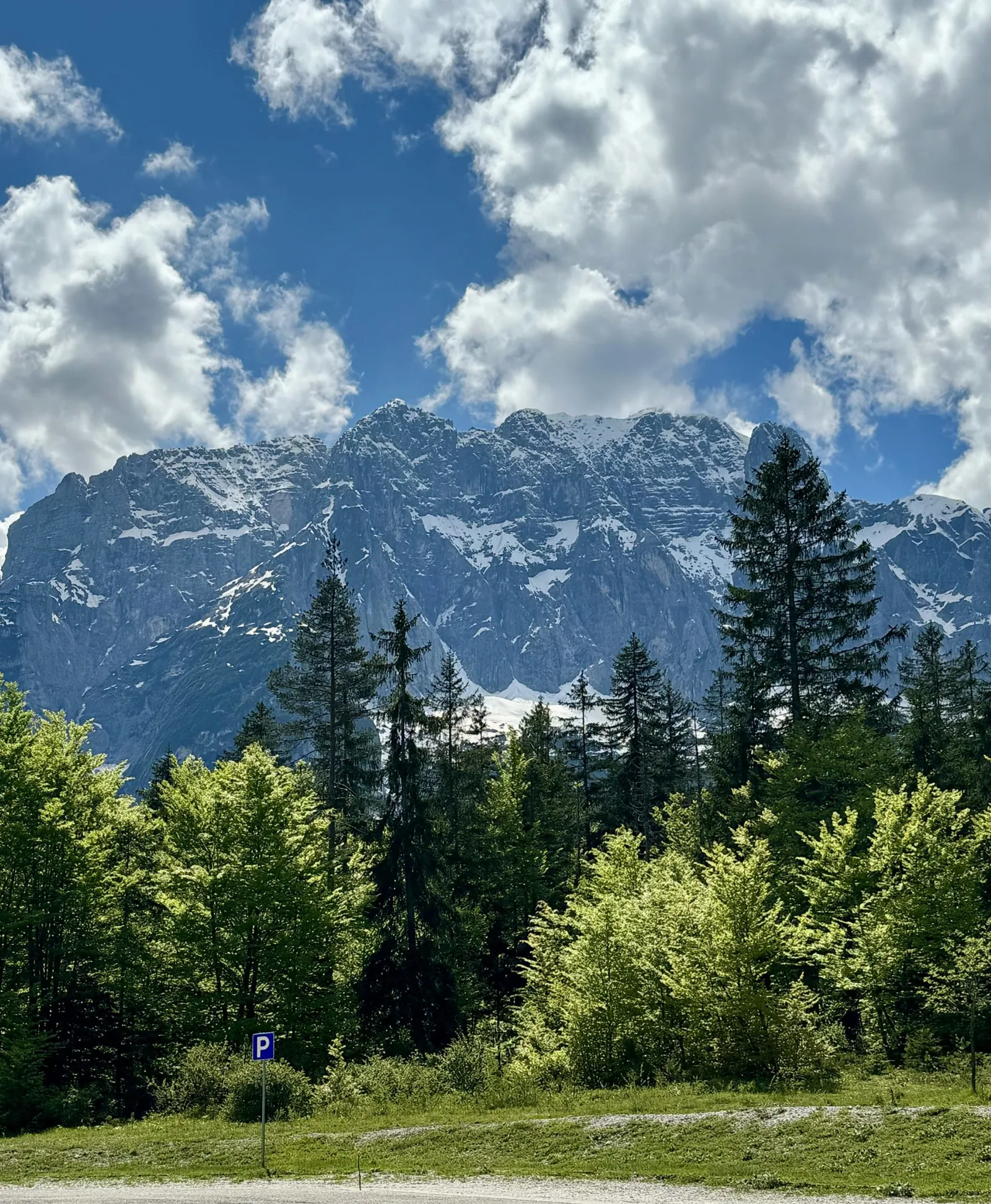 Schneebedeckter Felsgipfel über Nadelwald im Val Saisera, ein Parkplatzschild am Rand.