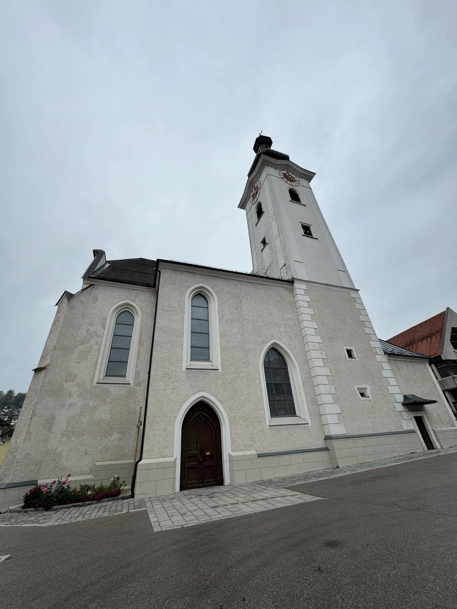 Weiße Kirche mit hohem Turm und Uhr in Ybbsitz unter bewölktem Himmel.