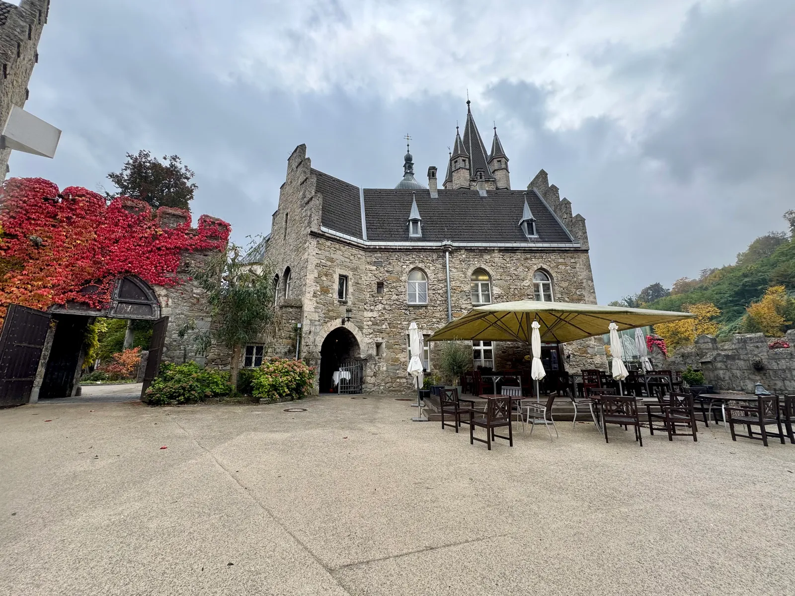 Schloss Rothschild mit gotischen Türmen und rotem Herbstlaub, im Hof ein Gastgarten.