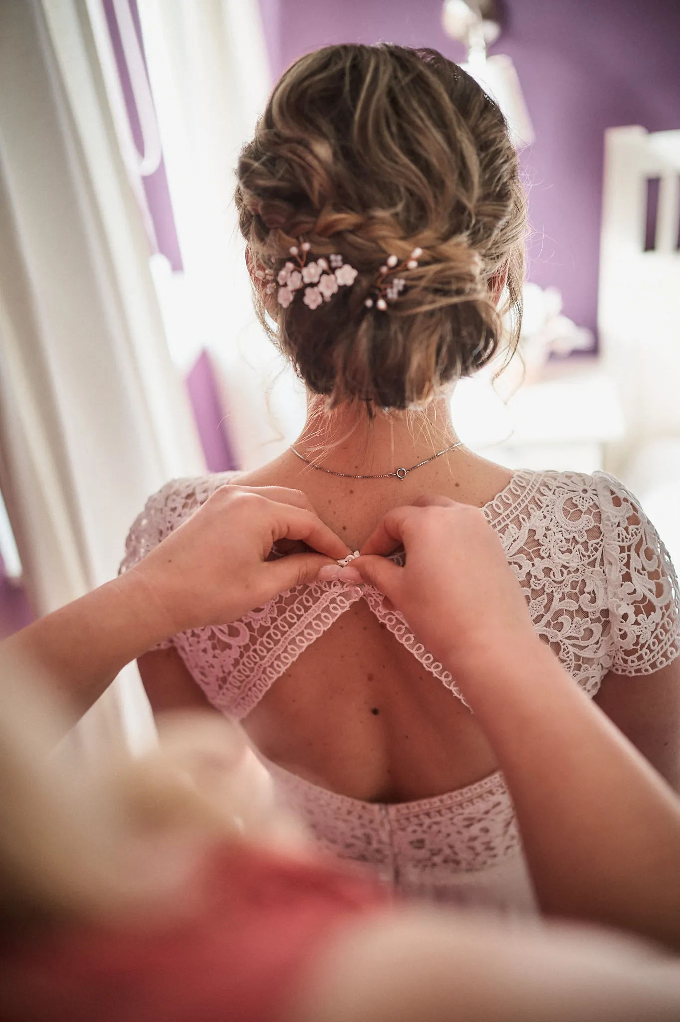 Nahaufnahme vom Rücken der Braut, wie die Trauzeugin das Kleid schließt