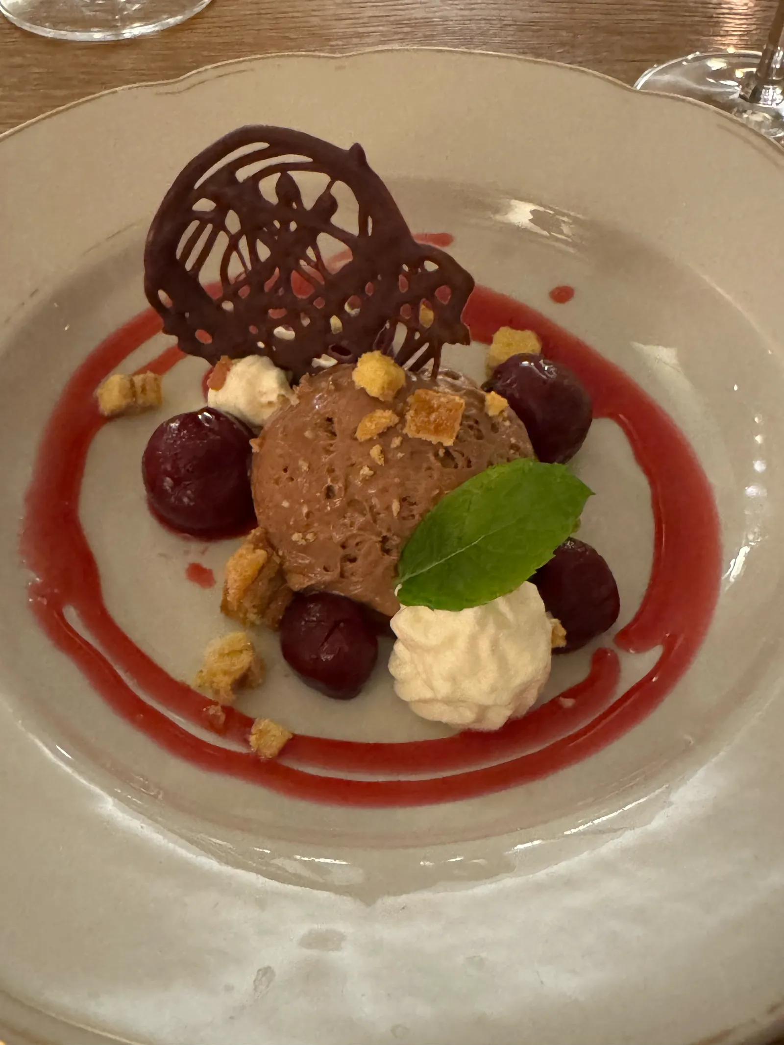 Schokoladedessert mit Kirschen, Schlagobers und Schokoladendekoration auf einem Teller.