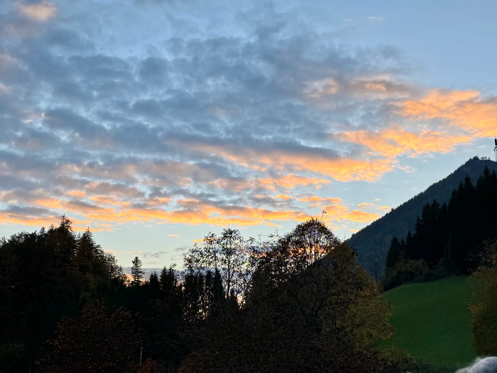 Abendrot mit orange leuchtenden Wolken über Bergsilhouetten und herbstlichen Bäumen.