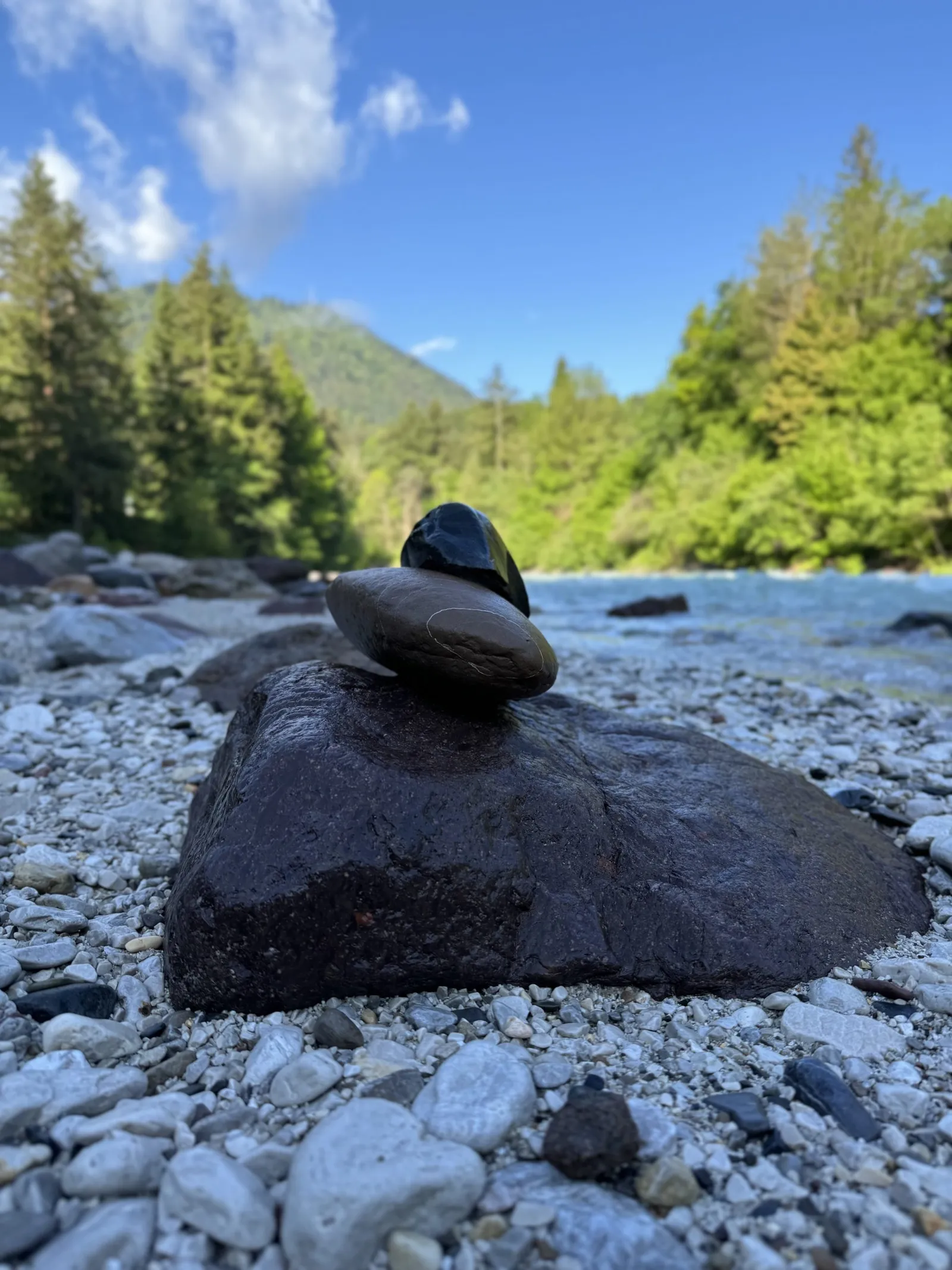 Kleine Steinpyramide auf einem Felsblock am Kiesufer eines Gebirgsflusses.