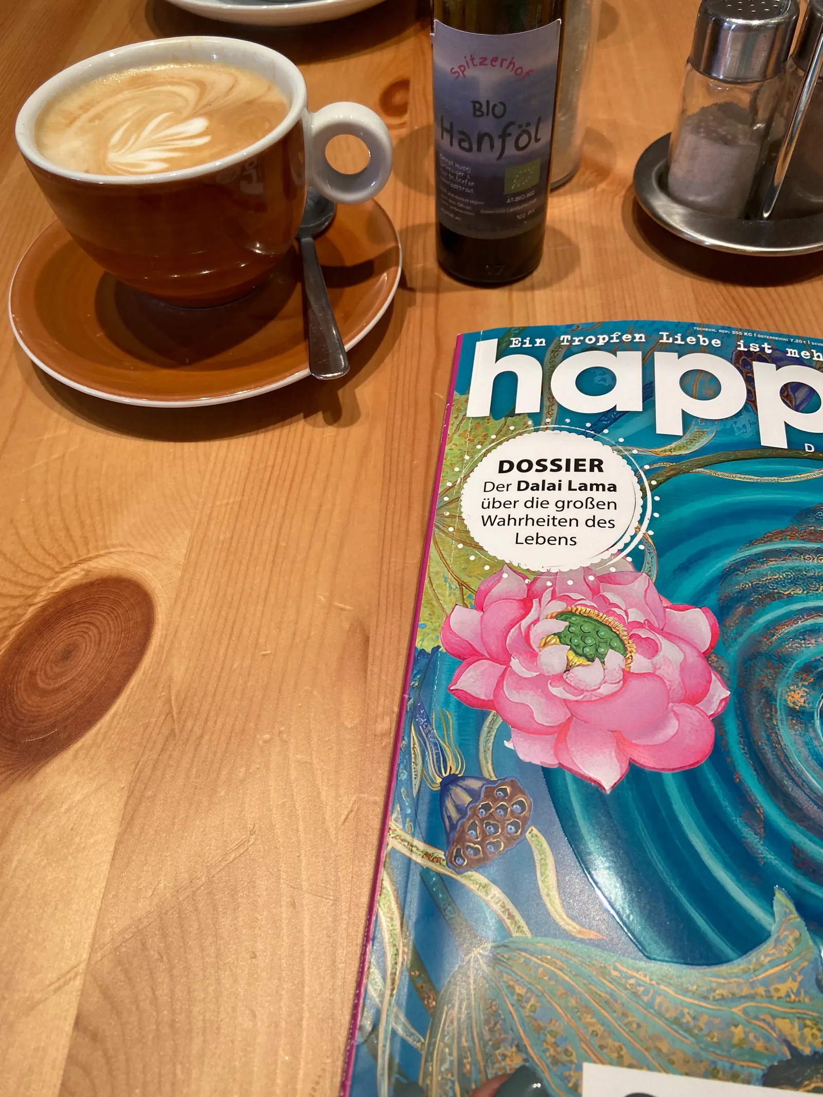 Cappuccino mit Latte Art neben einem Magazin auf einem Holztisch im Seelenfutter.