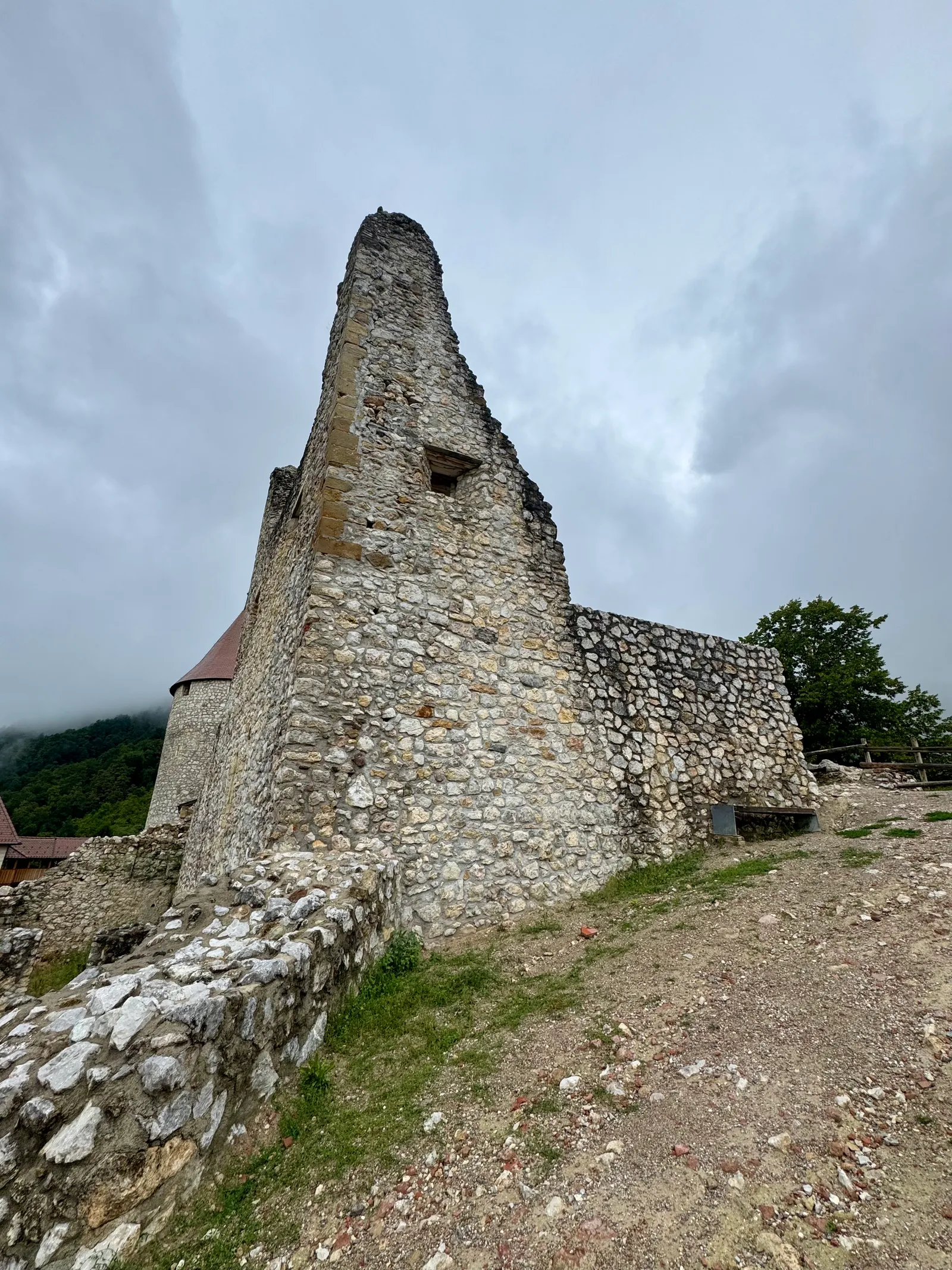 Hohe Ruinenmauer von Grad Žovnek von unten fotografiert unter bewölktem Himmel.