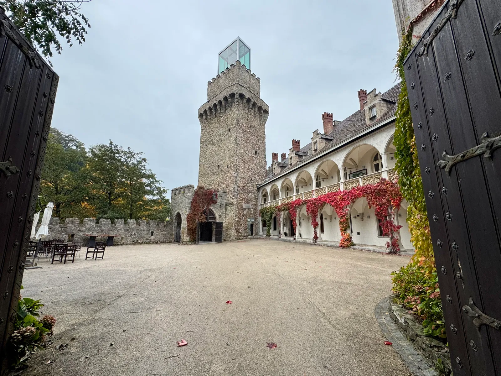 Innenhof von Schloss Rothschild mit Bergfried, rotem Herbstlaub und überwachsenem Arkadengang.