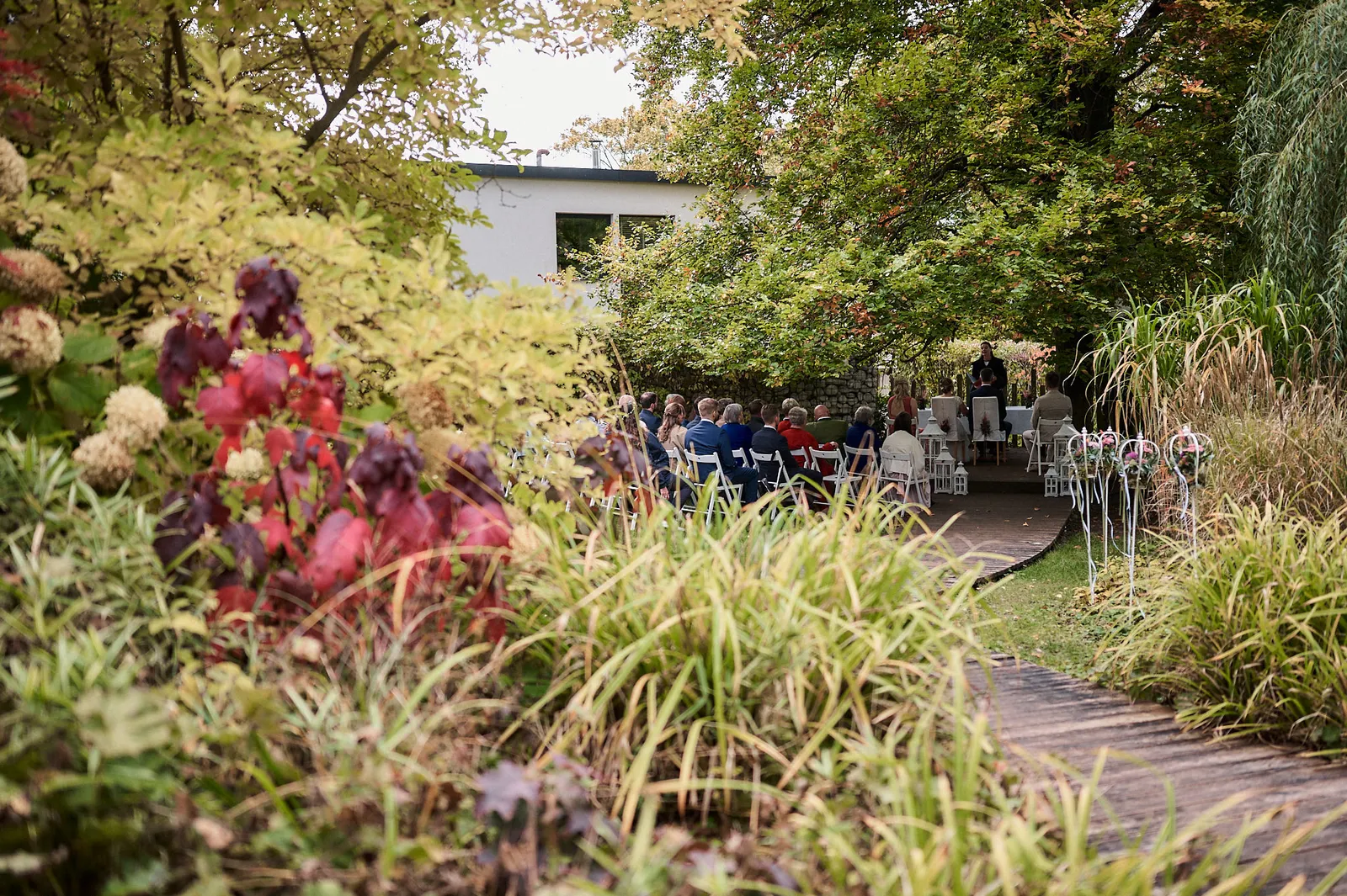 Standesamtliche Trauung im Freien: Gäste sitzen auf weißen Stühlen in einem herbstlichen Garten.