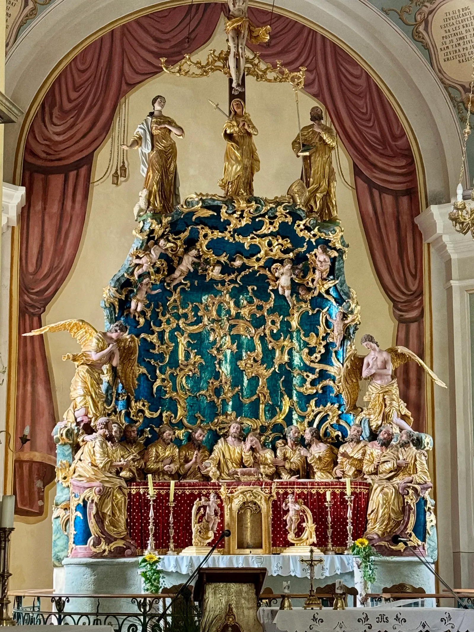 Vergoldeter Barockaltaraufbau mit Heiligenfiguren und Engeln auf blauem Ornamentgrund im Kircheninneren.