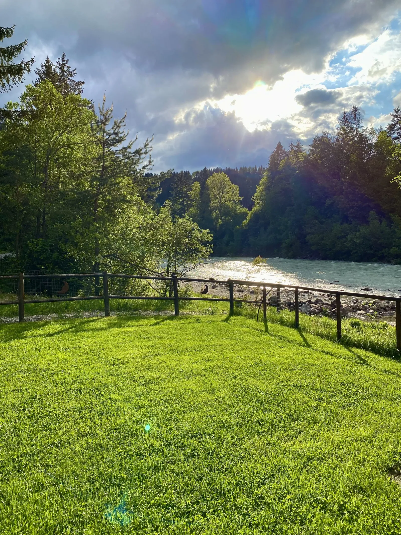 Eingezäunter Rasen am Flussufer mit Blick auf Wald und Himmel.