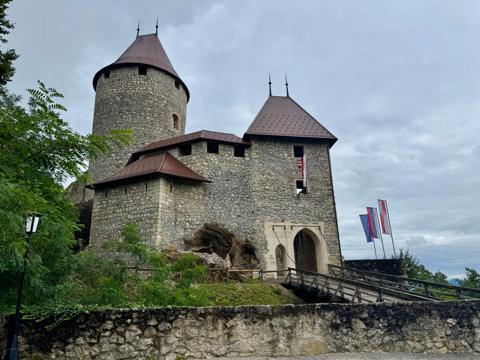 Das steinerne Eingangstor der Burgruine Grad Žovnek mit Türmen und Fahnen unter bewölktem Himmel.