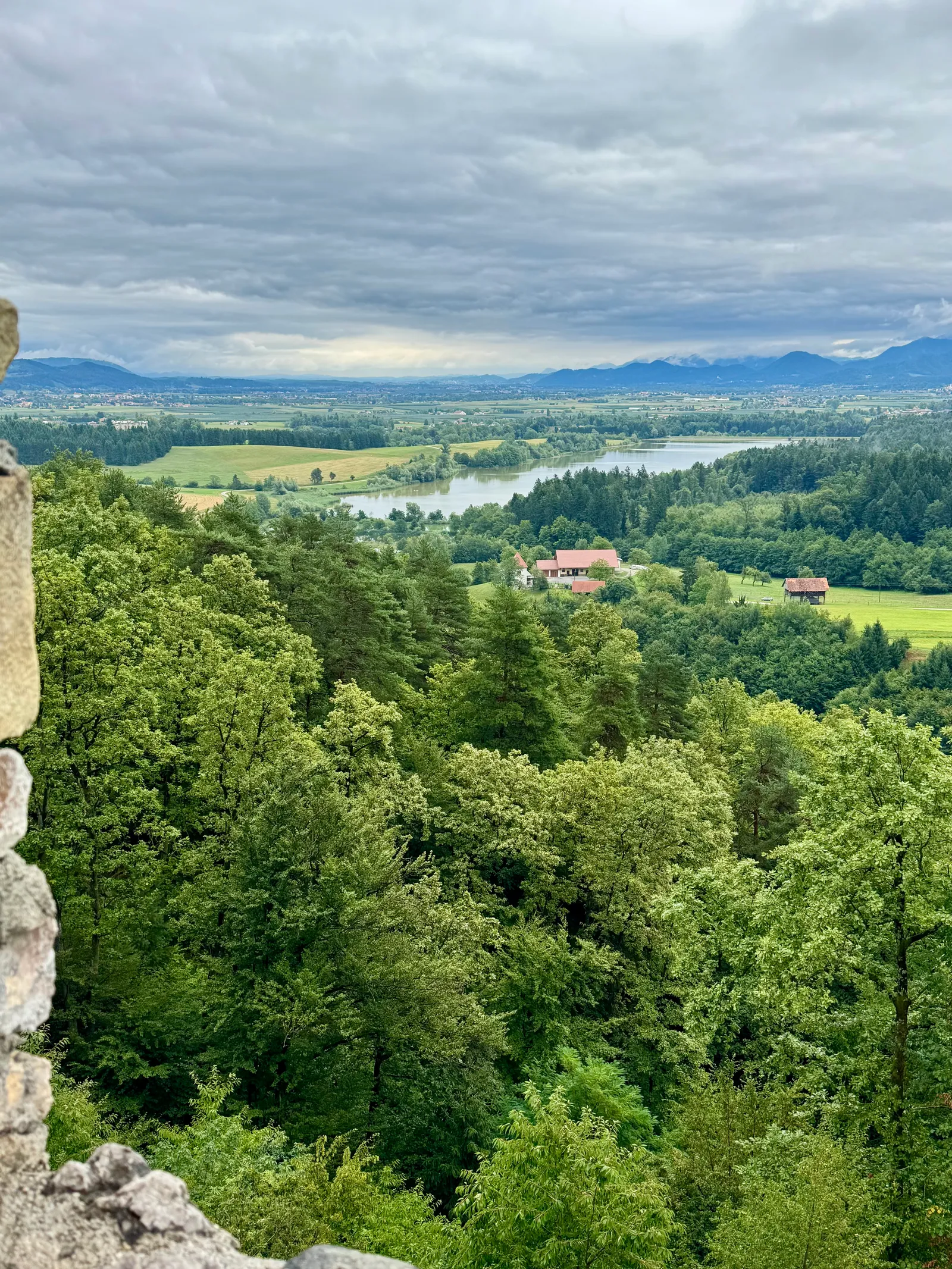 Ausblick von der Burgruine Grad Žovnek über Wald und einen See ins Tal mit Bergen am Horizont.