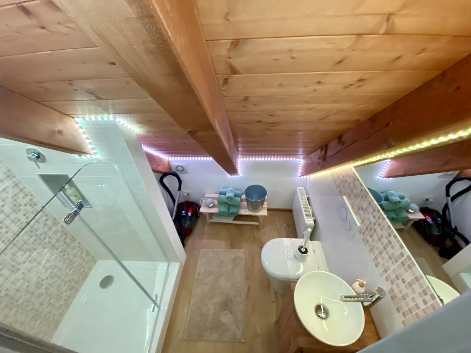 Kleines Badezimmer mit Dusche, Waschbecken und Bidet sowie bunter LED-Beleuchtung.