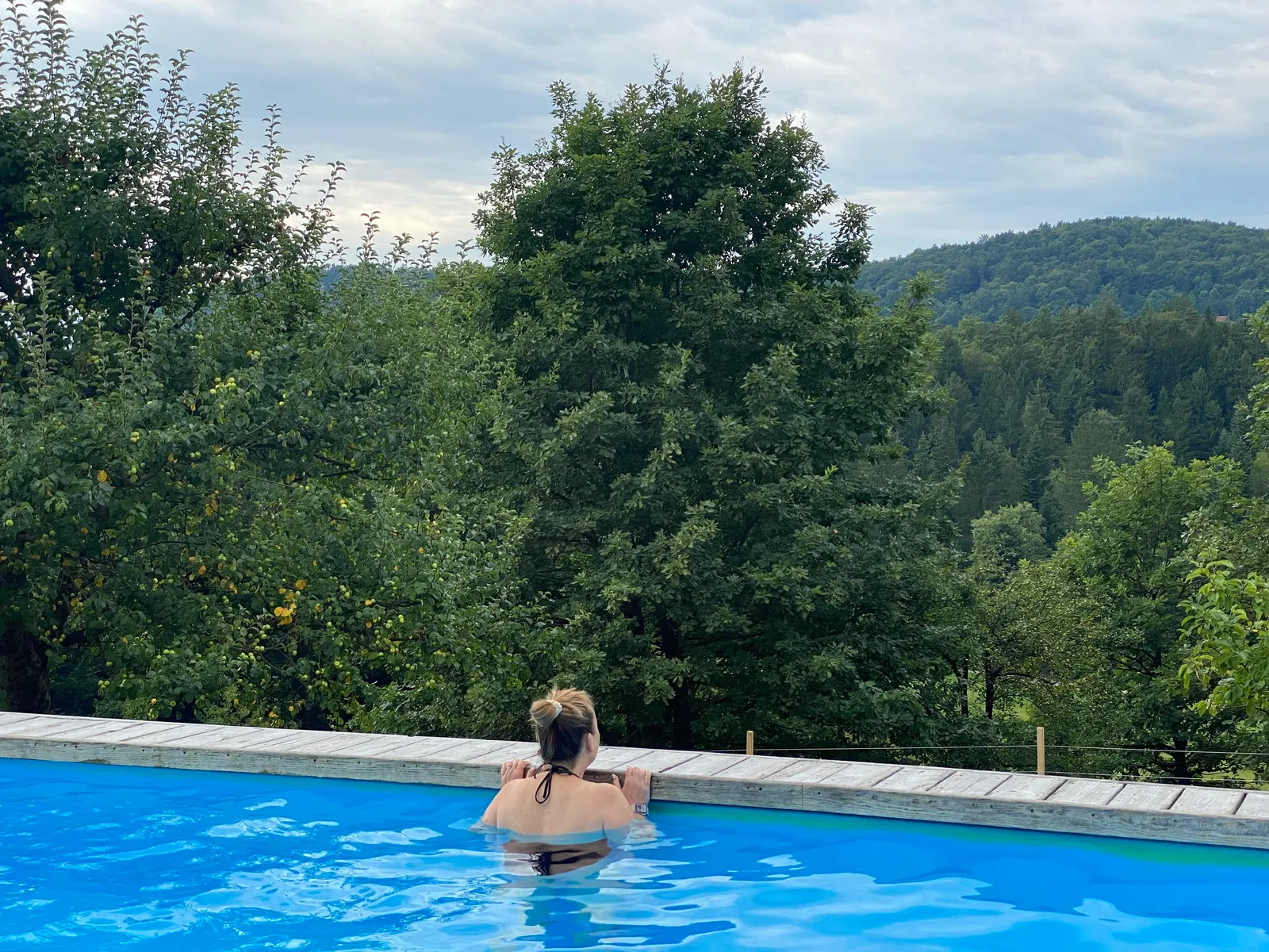 Babsi steht im Pool und blickt auf den bewaldeten Hügel dahinter.
