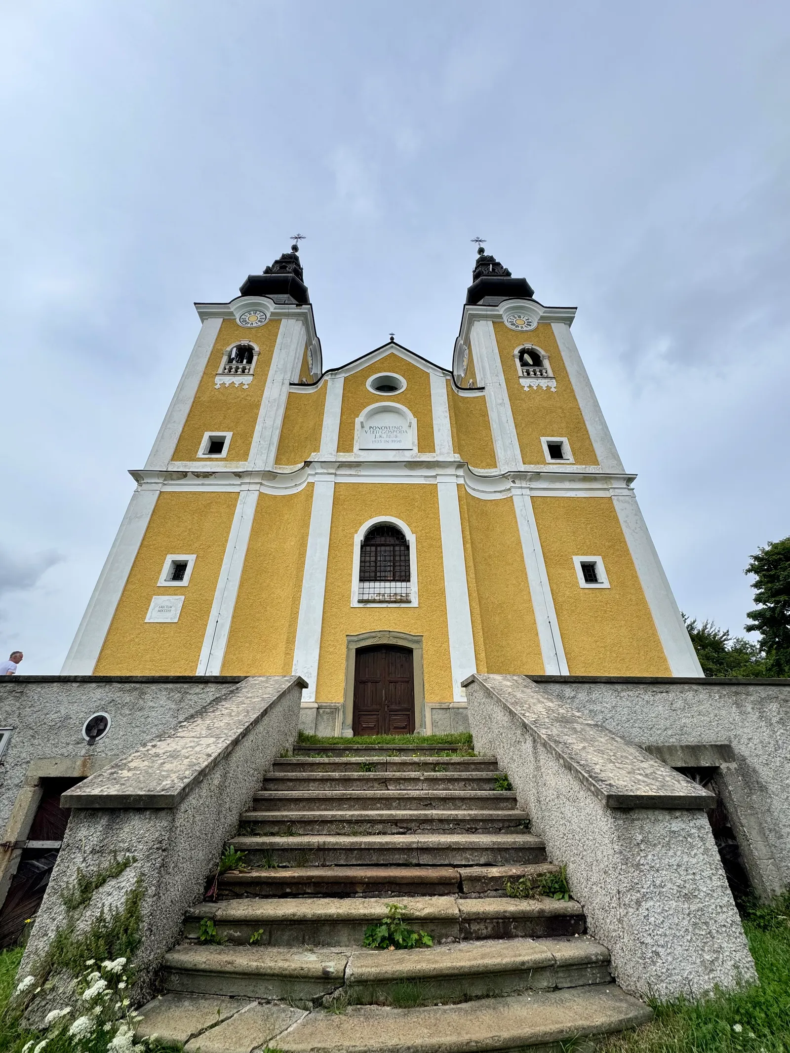 Gelbe Barockkirche mit zwei Türmen und Freitreppe, von unten fotografiert.