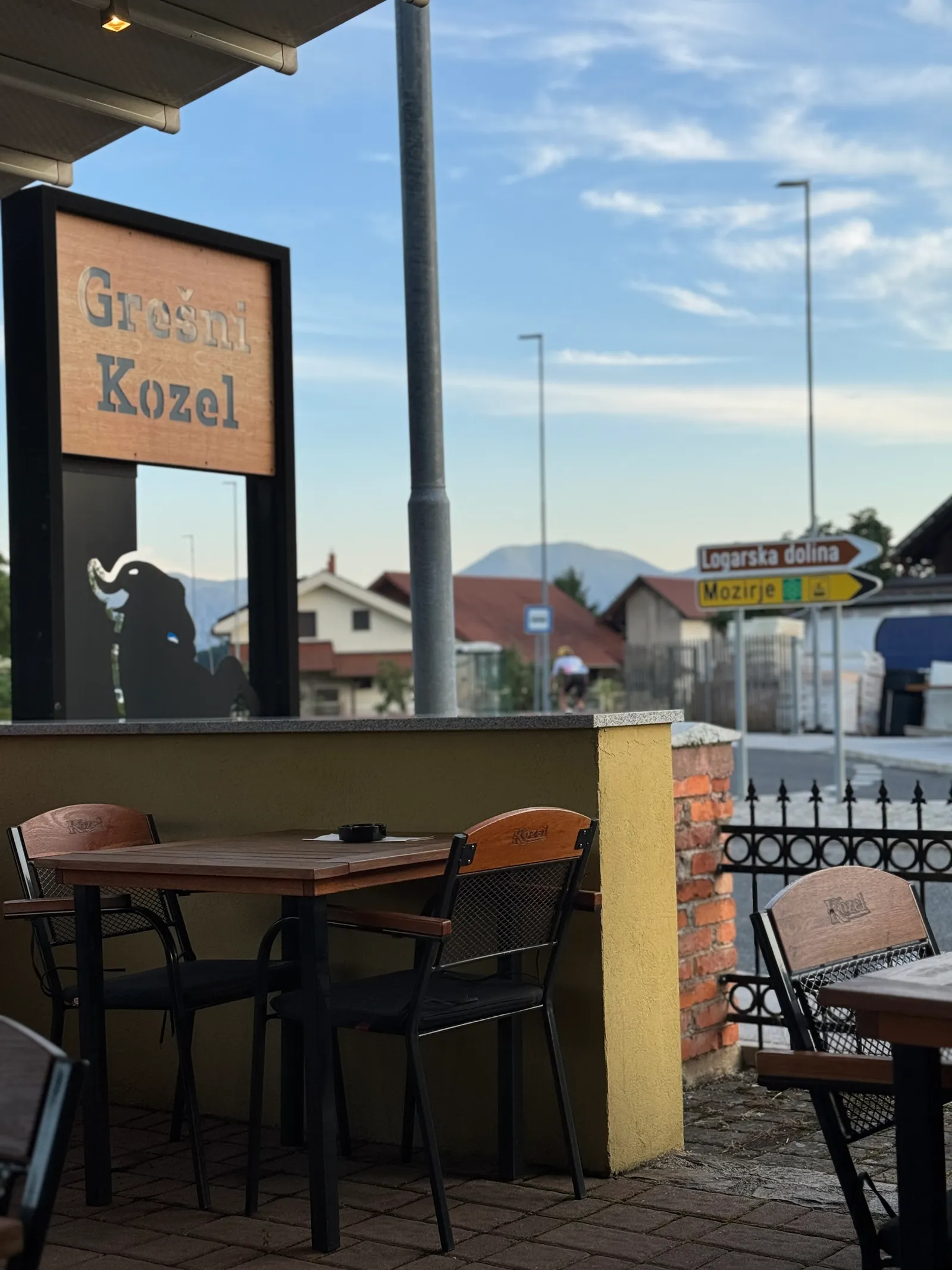 Außenterrasse des Restaurants Grešni Kozel mit Holztischen und Straßenschildern im Hintergrund.