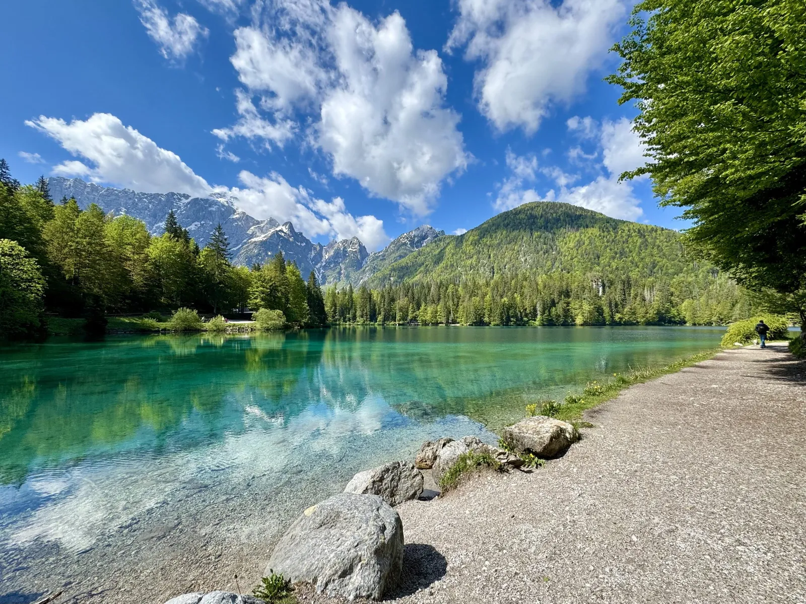 Türkisfarbener Lago di Fusine Inferiore mit Bergspiegelung und Uferpfad im Frühling.